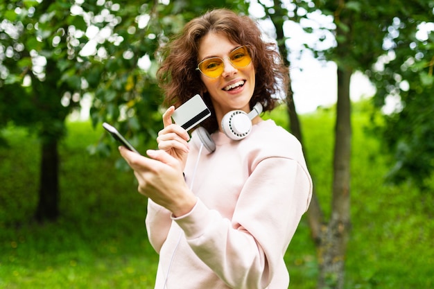 Muito jovem mulher caucasiana está envolvida em freelance no parque com cartão de crédito