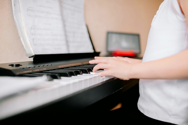 Muito jovem músico tocando piano digital clássico em casa durante as aulas on-line em casa