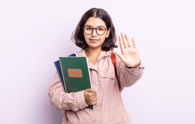 Muito jovem olhando sério mostrando a palma da mão aberta fazendo o aluno do gesto de parada com o conceito de livros