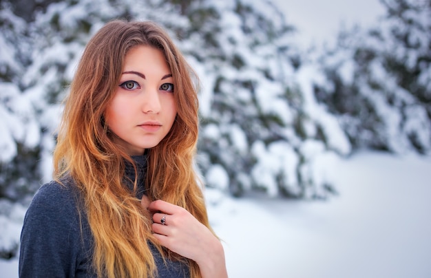 Muito jovem posando no inverno na floresta fria com pinheiros.