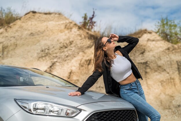 Muito jovem posando perto do carro em uma pedreira de areia