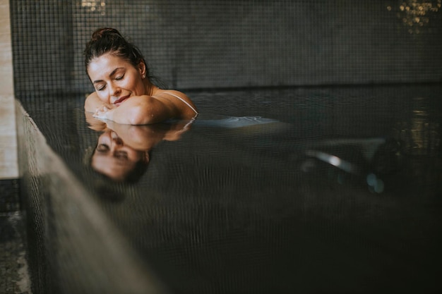 Muito jovem relaxante à beira da piscina interior