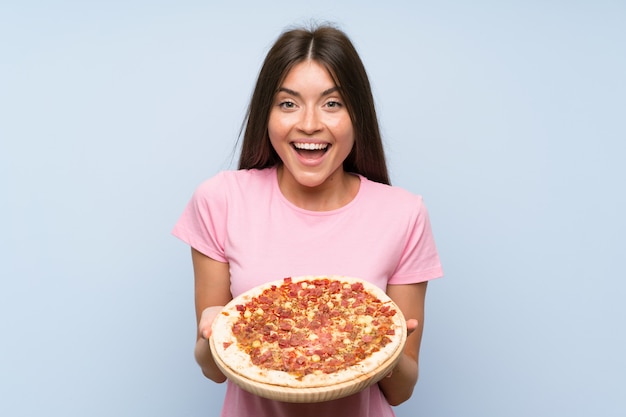 Muito jovem, segurando uma pizza sobre parede azul isolada