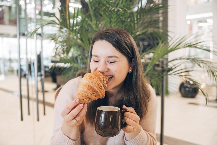 Muito jovem sentada com uma xícara de café em um café Mulheres adoráveis gostam de croissant no café da manhã