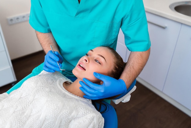 Muito jovem sentada na cadeira odontológica no centro médico enquanto médico profissional consertando seus dentes dentes saudáveis