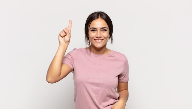 Muito jovem sorrindo alegremente e alegremente, apontando para cima com uma mão para copiar o espaço