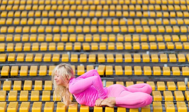 Muito jovem vestindo roupas esportivas rosa fazendo yoga asanas no parque em dia ensolarado em fundo amarelo