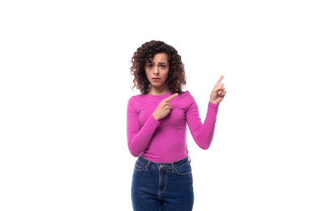 Foto muito sorridente jovem mulher morena encaracolada vestida com um colarinho roxo aponta com as mãos em