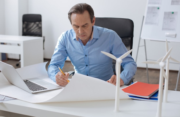 Muito trabalho a fazer. Engenheiro profissional concentrado sentado à mesa e desenhando o esquema enquanto trabalhava no projeto