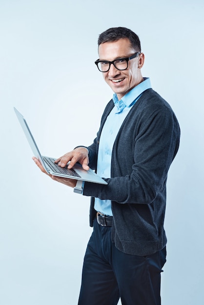 Muito trabalho a fazer. Foto recortada de um cavalheiro animado ganhando um traje casual elegante com um sorriso largo enquanto olha para a câmera e navega na Internet em um laptop.