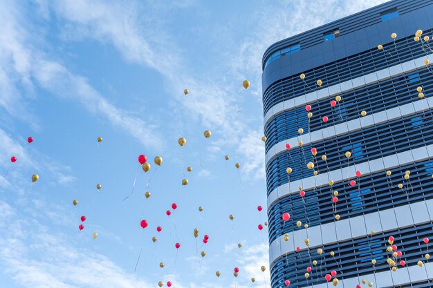 Muitos balões vermelhos e dourados voam ao lado de edifícios com céu azul e nuvens brancas