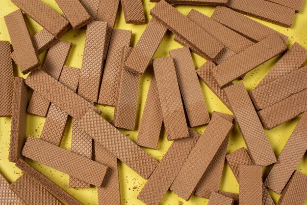 Muitos biscoitos de wafer de chocolate deitados irregularmente em um fundo amarelo, fundo de conceito