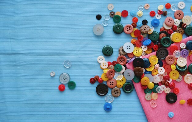 Muitos botões coloridos para roupas em um tecido azul Alfaiataria