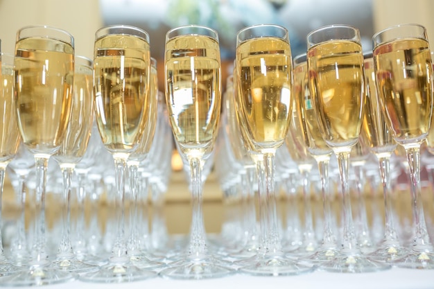 Muitos copos desfocados com champanhe na mesa da festa de recepção em fundo claro