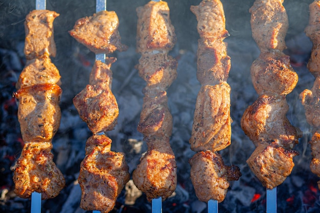 Muitos espetinhos de carne suculentos em uma fileira na grelha. pedaços de carne enfiados em espetos de metal na grelha ao pôr do sol. o processo de cozinhar kebabs com muita fumaça. cozinhando na natureza