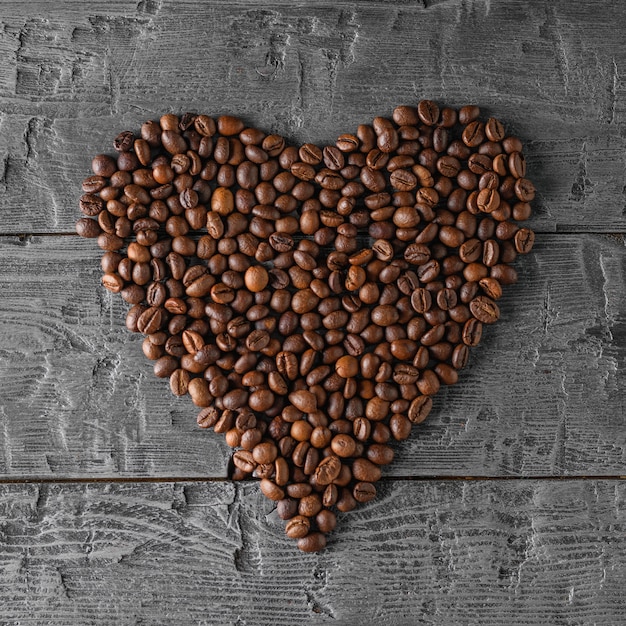 Muitos grãos de café dobrados em forma de coração em uma mesa de madeira preta. a vista do topo. postura plana. grãos para a preparação da bebida popular.