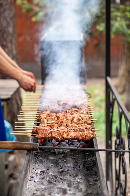 Muitos kebabs seguidos na grelha. espetadas amarradas em espetos de madeira  em um café de rua. o processo de cozinhar kebabs com muita fumaça.