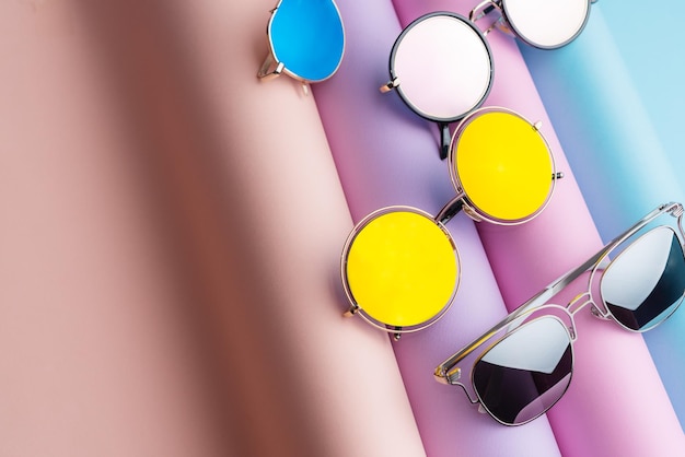 Muitos óculos de sol de moda coloridos colocados em fundo de papel pastel colorido