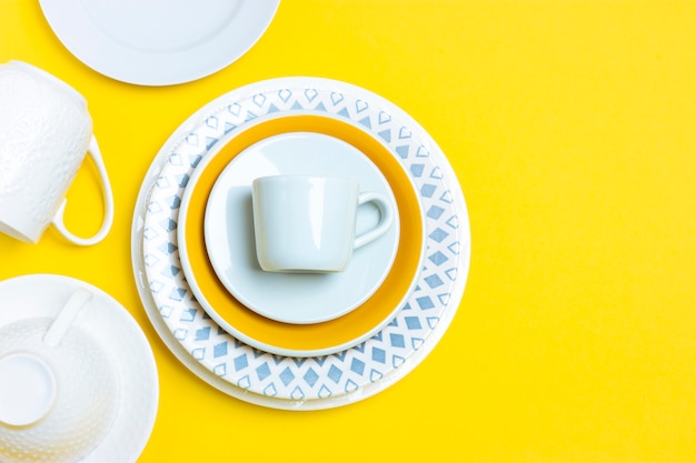 Muitos pratos de cerâmica diferentes, pares de café vazios, pratos, xícaras em um fundo amarelo brilhante. Ornamentos abstratos em objetos