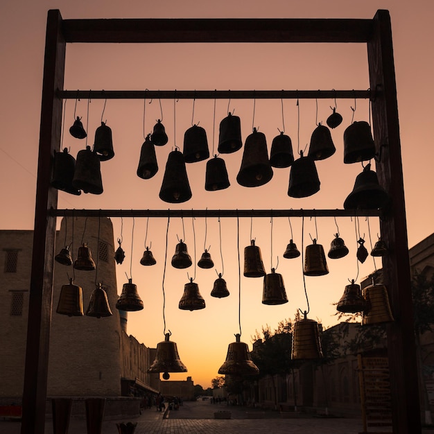 Muitos sinos pequenos penduram no mercado na cidade velha contra o pano de fundo do céu do sol Bukhara Uzbequistão