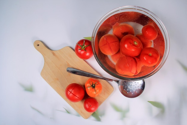 muitos tomates escaldados em uma tigela com água, prontos para descascar