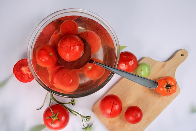 muitos tomates escaldados em uma tigela com água, prontos para descascar