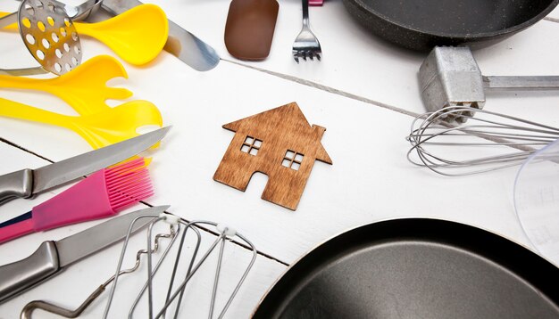 Muitos utensílios de cozinha diferentes na mesa de madeira e uma casinha de madeira entre eles