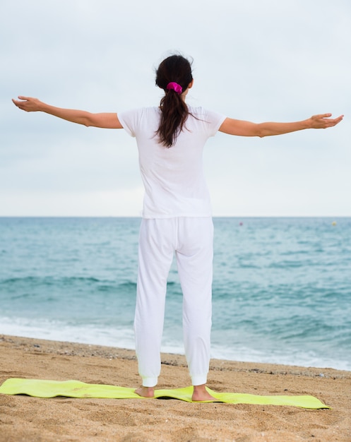 Foto mujer 20-30 años de edad se encuentra y practicar la meditación en camiseta blanca en la playa.