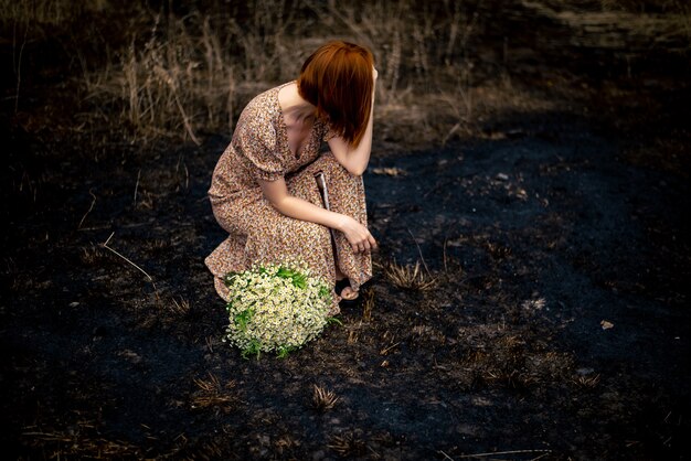 Mujer de 40 años con un ramo de flores silvestres en la tierra quemada, concepto de agotamiento psicológico