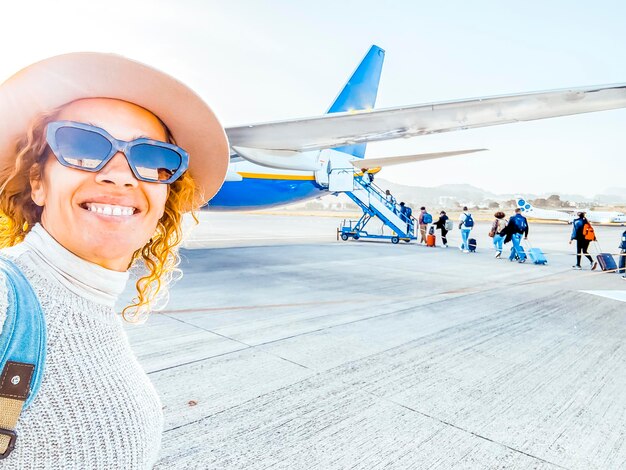 Foto mujer de 50 años con sombrero y gafas de sol se toma una selfie antes de abordar el avión mujer feliz y solitaria toma una foto de recuerdo