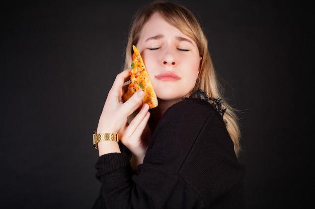 Una mujer abraza con cariño una rebanada de pizza, sobre un fondo negro.