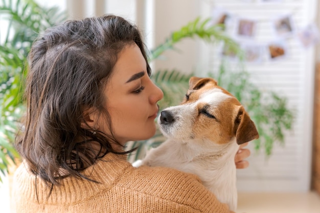 Foto mujer abraza a un lindo perrito tendido en sus brazos en casa en primer plano confianza