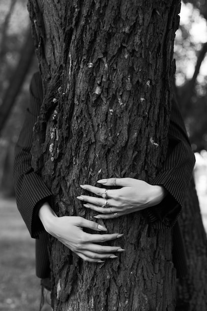 Una mujer abrazando un árbol con las manos en el tronco.