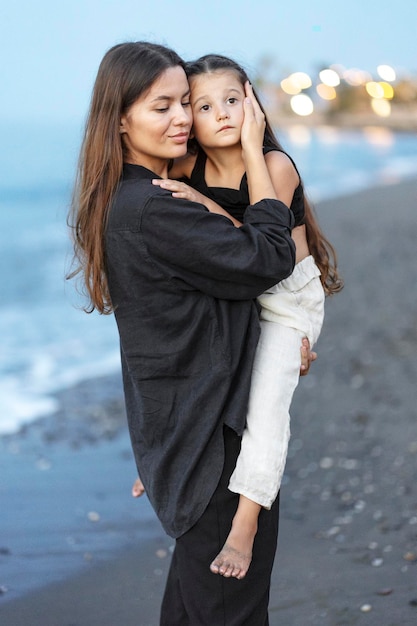 mujer abrazando a su hija pequeña con los ojos cerrados mientras camina por la playa foto en blanco y negro