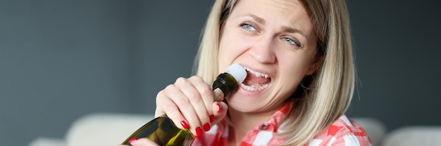 La mujer abre la botella de champán con los dientes. Concepto de alcoholismo femenino