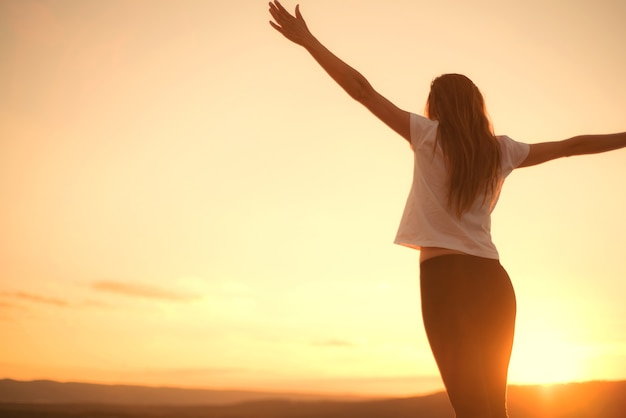 La mujer abre los brazos debajo de la puesta del sol. Concepto de vida saludable.