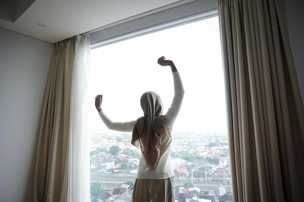 Mujer abriendo cortinas en el dormitorio por la mañana para estirar el cuerpo