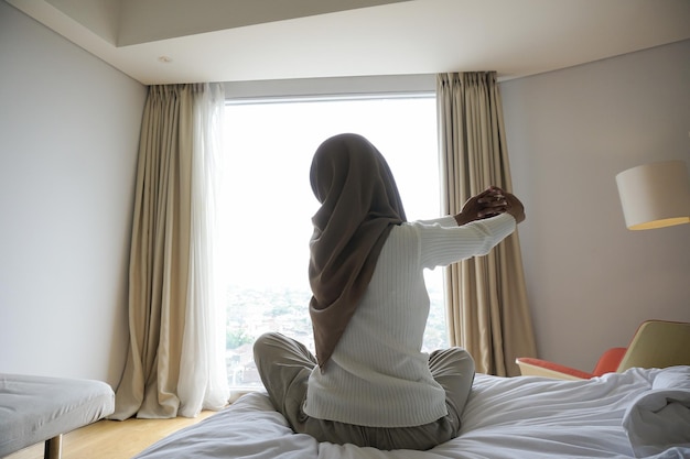 Mujer abriendo cortinas en el dormitorio por la mañana para estirar el cuerpo