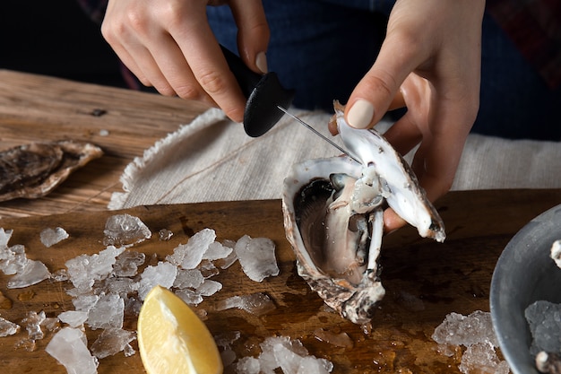 Mujer abriendo ostras crudas con un cuchillo en la mesa, primer plano