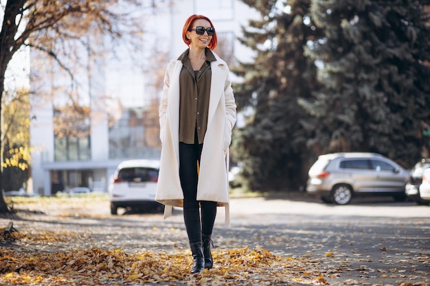 Mujer con abrigo beige de pie en el parque de otoño