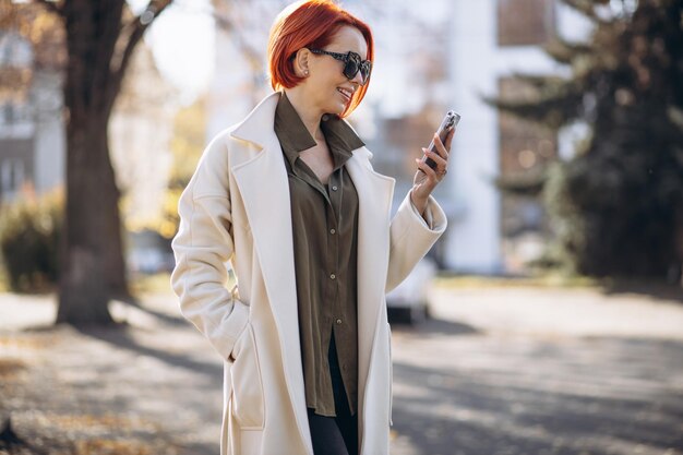 Mujer con abrigo beige de pie en el parque de otoño