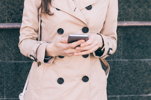 Mujer en un abrigo beige sostiene un teléfono móvil en manos