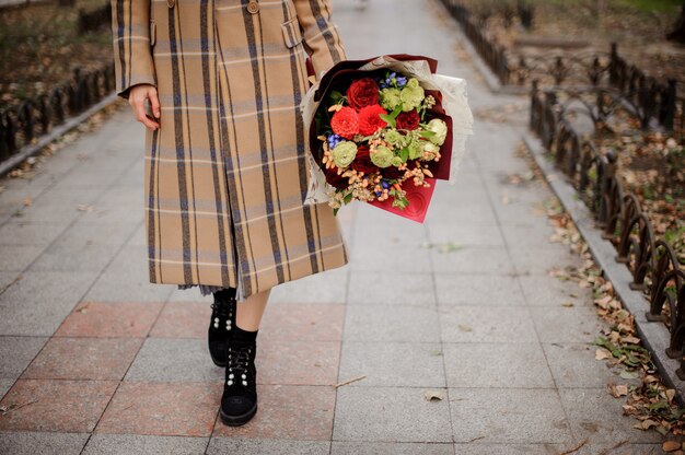 Mujer con abrigo a cuadros caminando con un ramo de flores en el callejón