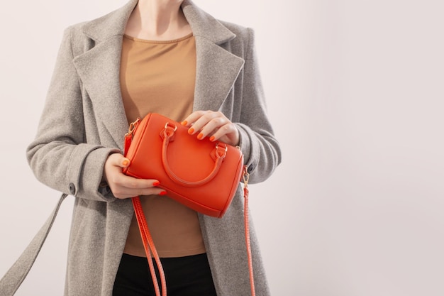 Mujer en abrigo gris con bolso naranja sobre fondo blanco.