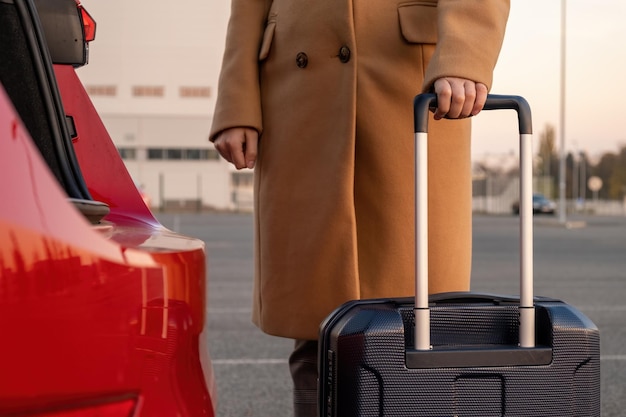 Una mujer con un abrigo marrón se para con una maleta cerca de un autobús rojo de un concepto de aeropuerto