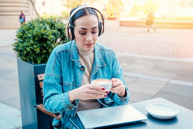 Mujer con abrigo de mezclilla y auriculares bebiendo café y escuchando música Concepto de estilo de vida