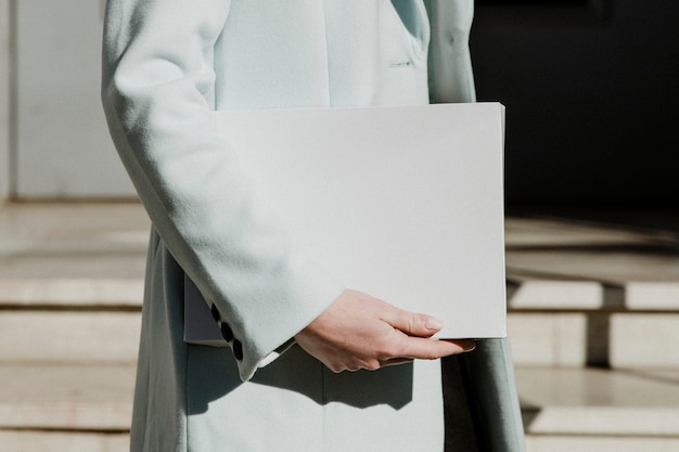 Mujer en un abrigo que lleva una caja blanca en frente de un edificio