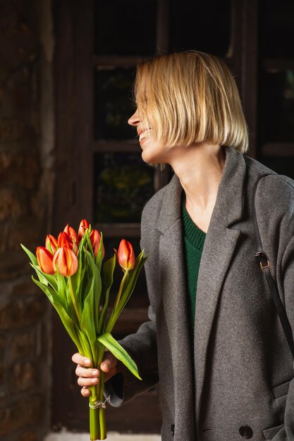 Mujer en un abrigo con un ramo de tulipanes sobre un fondo oscuro Regalo de vacaciones