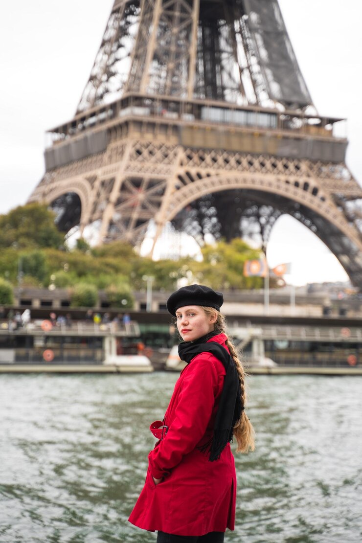 Foto una mujer con un abrigo rojo se para frente a la torre eiffel en parís, francia.