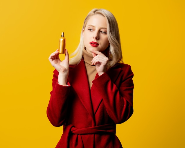 Mujer en abrigo rojo con perfume en pared amarilla